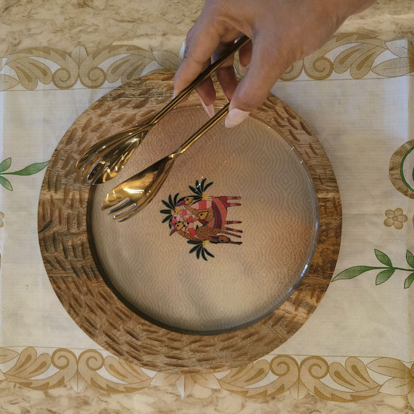 Luxury golden serving tong held over decorative plate with wooden rim on patterned tablecloth