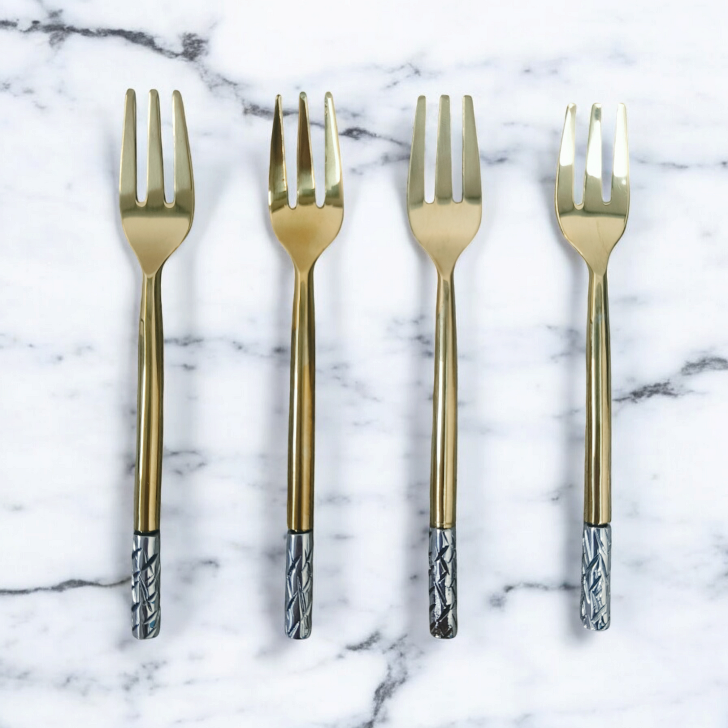 Elegant fruit fork set with gold tines and textured silver handles laid out on marble surface